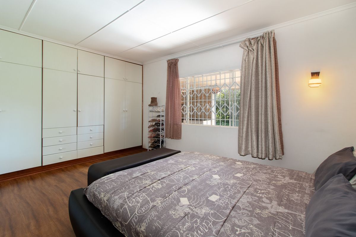 A bedroom featuring laminate flooring, extensive built-in cupboard storage, and a window fitted with a security gate.