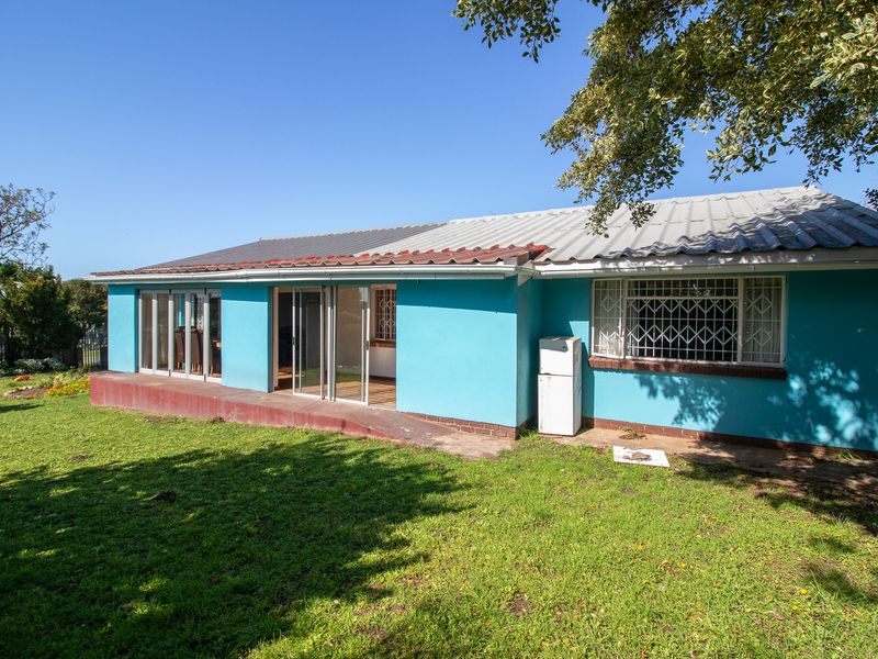 Rear view of the house featuring a concrete patio, sliding glass doors, and security-barred windows set against a spacious garden area.