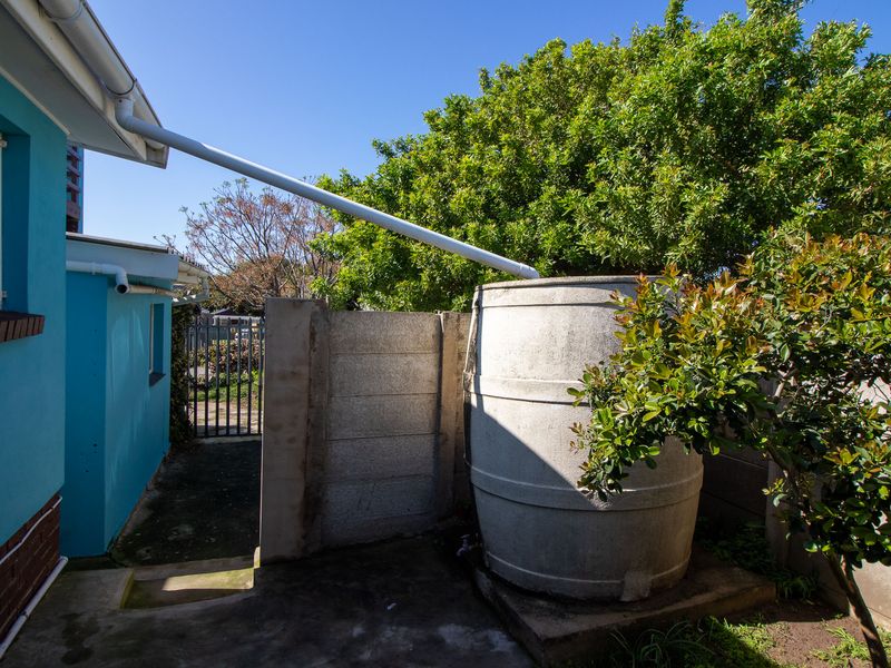 Rear exterior area featuring a rainwater collection tank connected to the building's guttering system, set against a concrete boundary wall.