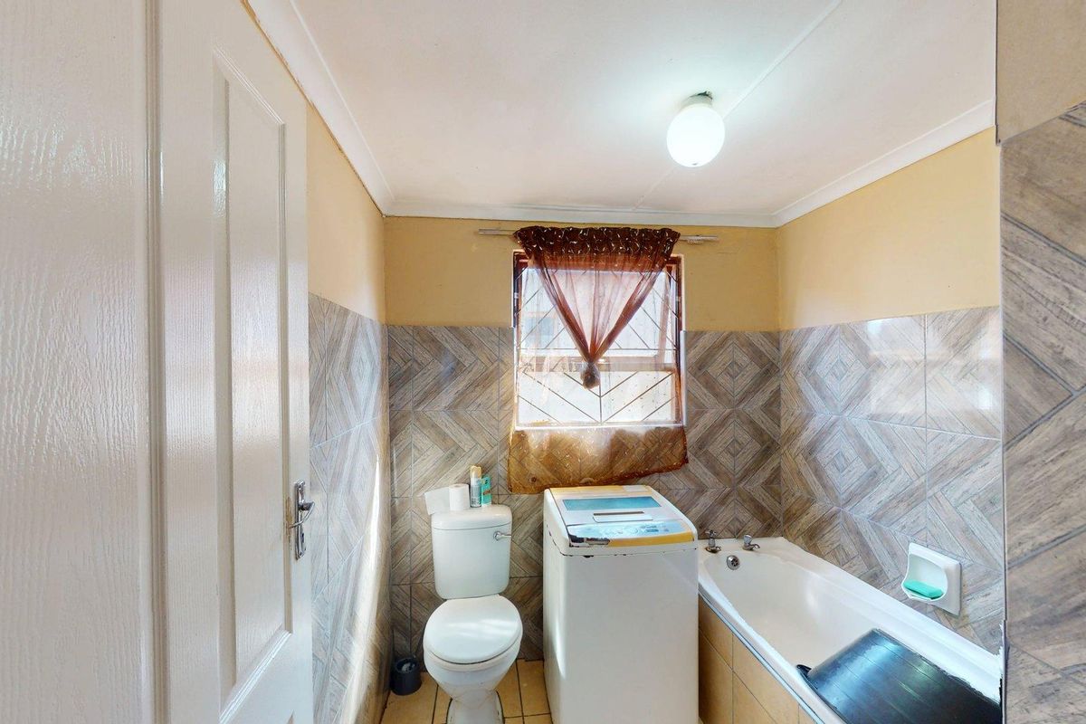 A functional bathroom featuring a bathtub, toilet, and tiled wall finishes with a window providing natural light.