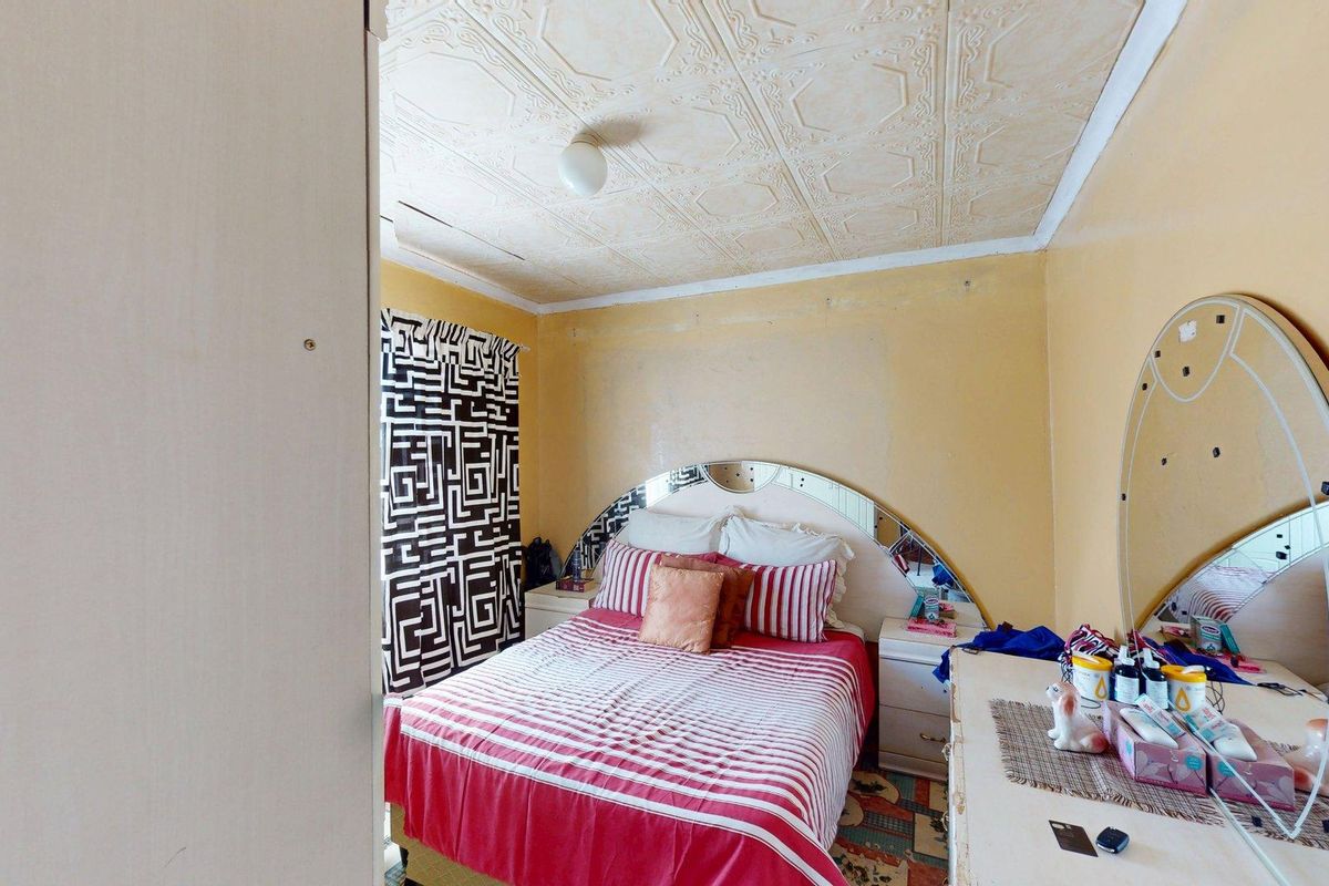 A bedroom featuring a decorative pressed metal ceiling and yellow wall finishes, requiring cosmetic updates and repairs to the ceiling and walls.