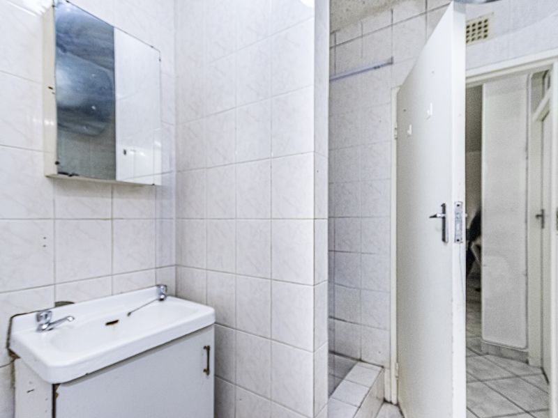 A dated bathroom featuring a vanity basin, wall-mounted mirror cabinet, and a tiled shower area, requiring cosmetic updates to modernize the space.