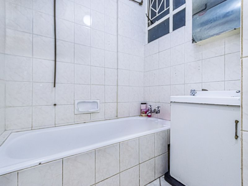 A dated bathroom featuring a standard bathtub, tiled walls, and a basin. The space requires cosmetic updates to improve its overall condition and appeal.