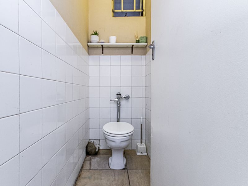 A compact bathroom featuring white wall tiles, a flush toilet, and a small high-level window.
