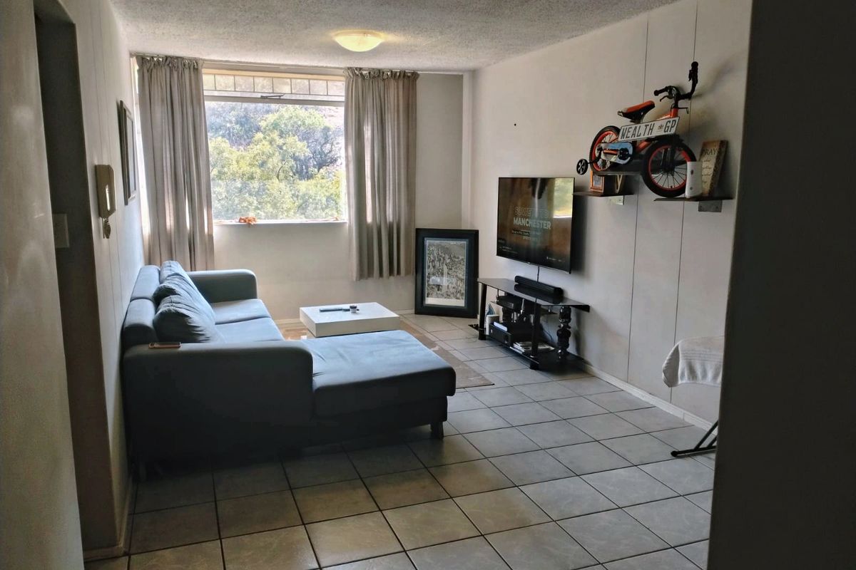 A living room featuring tiled flooring and a large window, providing natural light. The space offers a functional layout for relaxation.