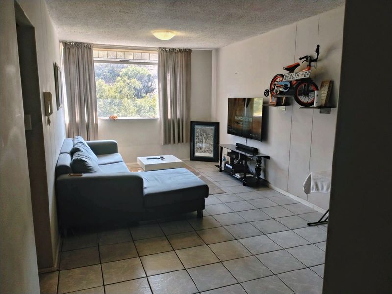 A living room featuring tiled flooring and a large window, providing natural light. The space offers a functional layout for relaxation.