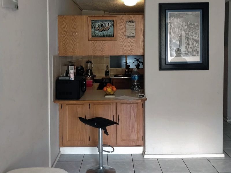 A compact, dated kitchen area featuring wood-look laminate cabinetry, tiled backsplash, and ceramic floor tiles, offering potential for a modern renovation.