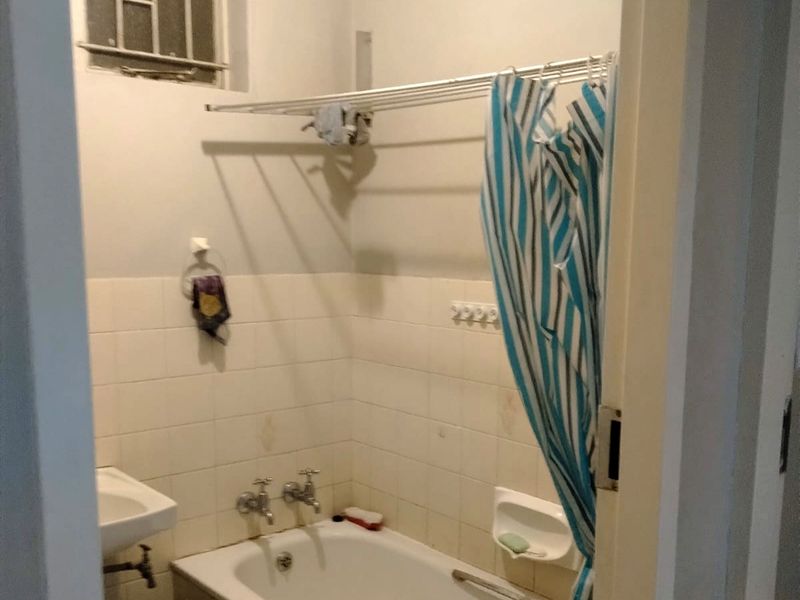 A compact bathroom featuring a bathtub, wall-mounted basin, and tiled splashback, currently showing signs of age and wear.
