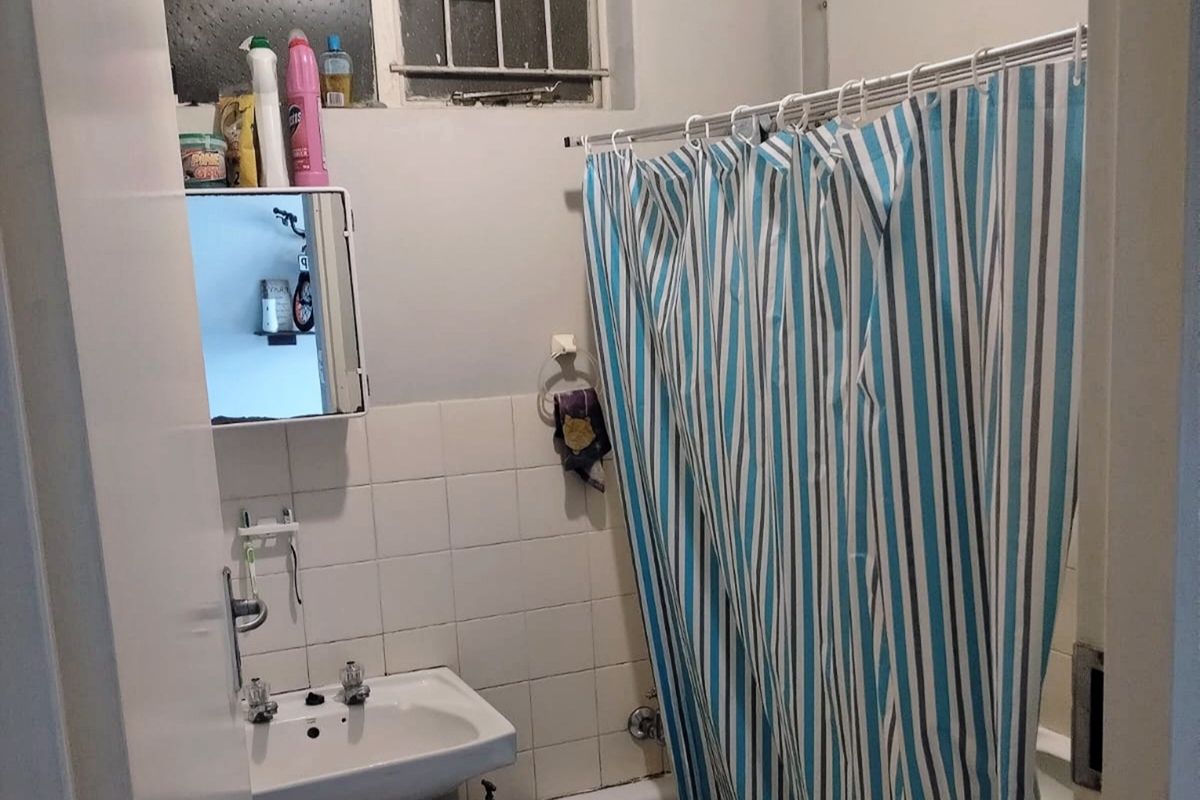 A compact bathroom featuring a pedestal basin, bathtub with shower curtain, and a wall-mounted medicine cabinet, requiring cosmetic updates to modernize the space.
