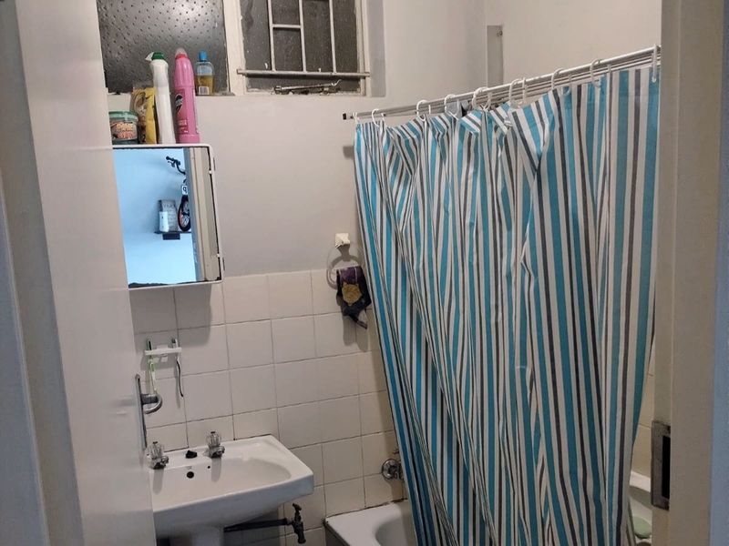 A compact bathroom featuring a pedestal basin, bathtub with shower curtain, and a wall-mounted medicine cabinet, requiring cosmetic updates to modernize the space.