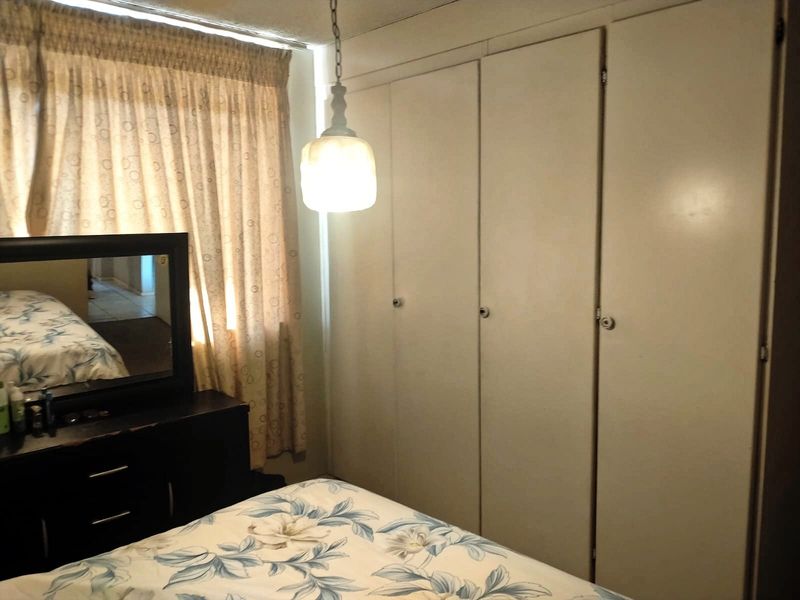A bedroom featuring built-in cupboards and a pendant light fixture, requiring cosmetic updates to modernize the space.