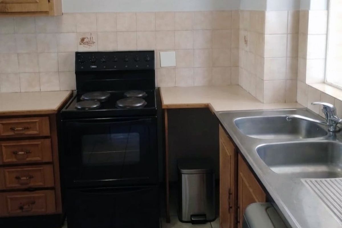 A functional kitchen featuring wooden cabinetry, laminate countertops, a double bowl stainless steel sink, and a freestanding electric stove with tiled splashback.