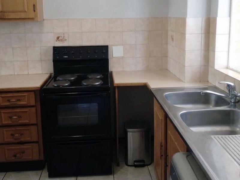 A functional kitchen featuring wooden cabinetry, laminate countertops, a double bowl stainless steel sink, and a freestanding electric stove with tiled splashback.