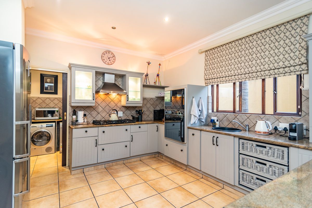 A well-maintained kitchen featuring grey cabinetry, granite countertops, a gas hob with extractor, and a separate scullery area with laundry facilities.