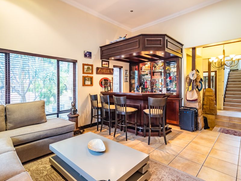 A well-appointed home bar area featuring custom dark wood cabinetry, integrated shelving, and tiled flooring, seamlessly connected to the living space and staircase.