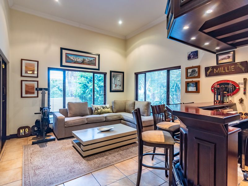 A spacious entertainment area featuring a built-in bar, tiled flooring, and high ceilings with recessed lighting, creating a comfortable space for hosting.