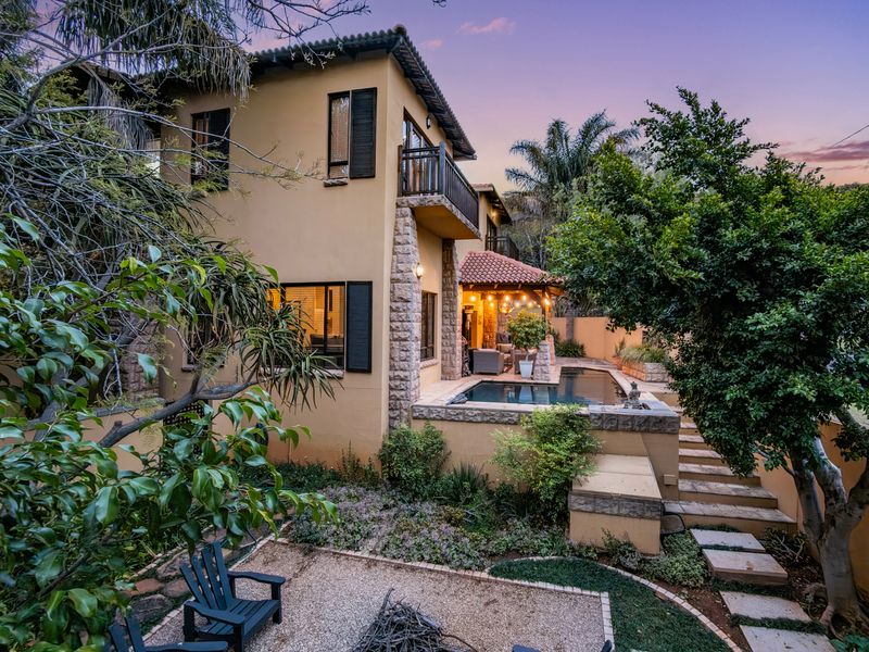 Rear view of a multi-story home featuring a swimming pool, covered patio, stone accents, and a well-maintained landscaped garden at dusk.