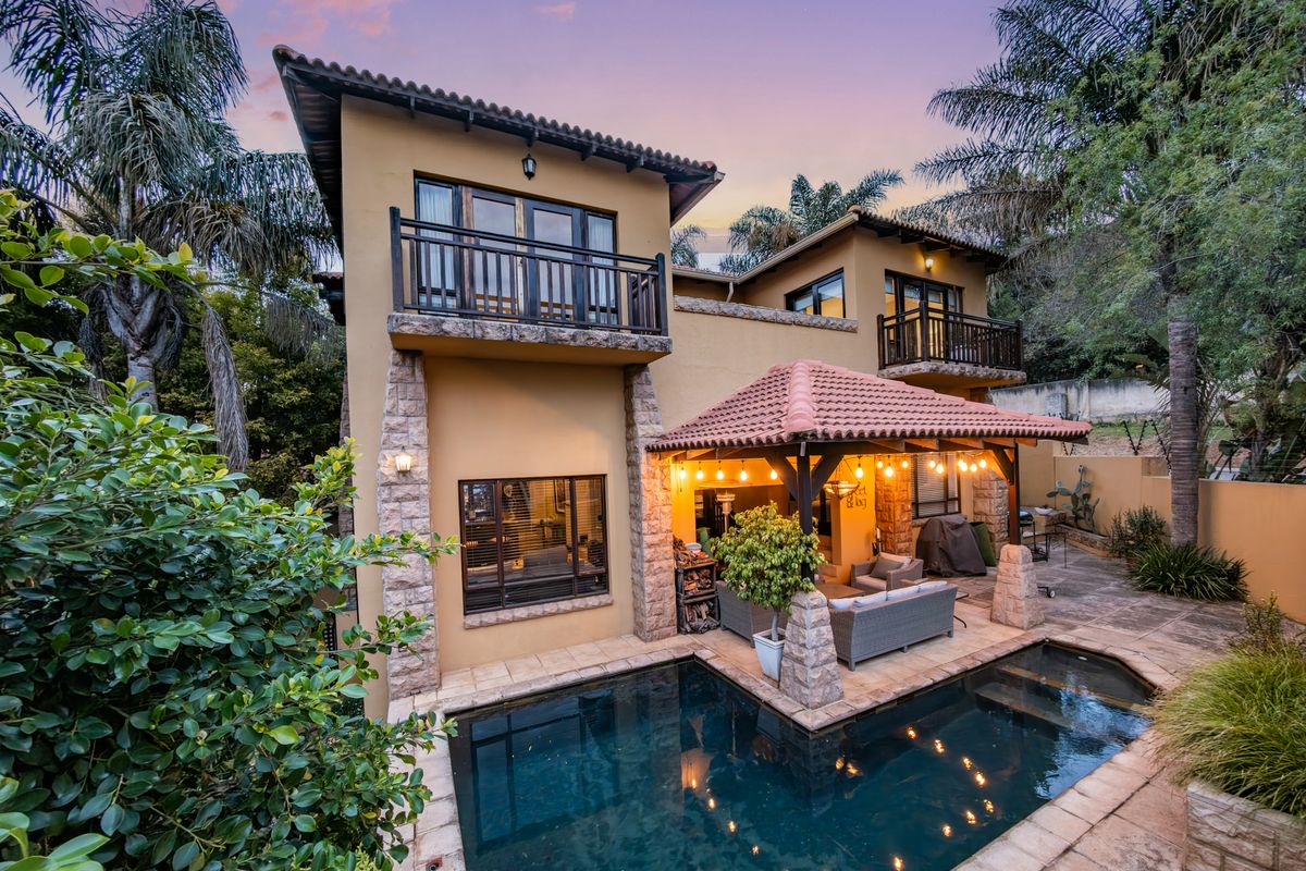 Rear view of a two-story house featuring a swimming pool, a covered patio area with lighting, and upper-level balconies.