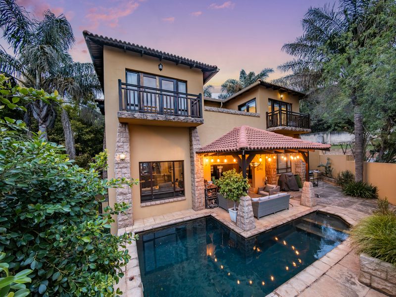 Rear view of a two-story house featuring a swimming pool, a covered patio area with lighting, and upper-level balconies.