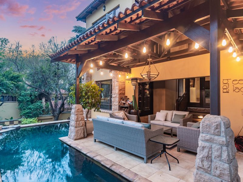 A covered outdoor patio featuring a timber pergola and stone-clad pillars, overlooking a swimming pool, perfect for relaxed outdoor entertaining.