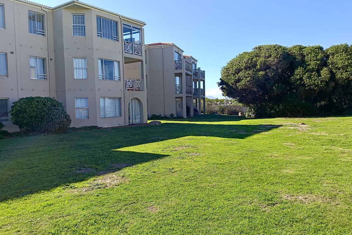 Rear view of the apartment complex featuring multi-story balconies, sliding glass doors, and a well-maintained communal lawn area.