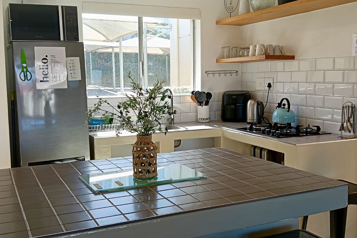 A functional kitchen featuring a tiled island, subway tile backsplash, floating timber shelving, and integrated gas hob with stainless steel sink.