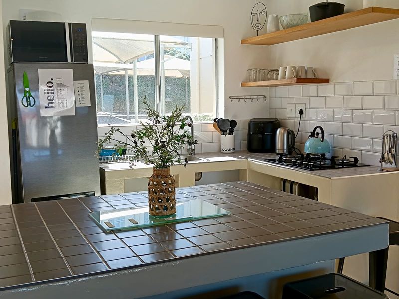 A functional kitchen featuring a tiled island, subway tile backsplash, floating timber shelving, and integrated gas hob with stainless steel sink.