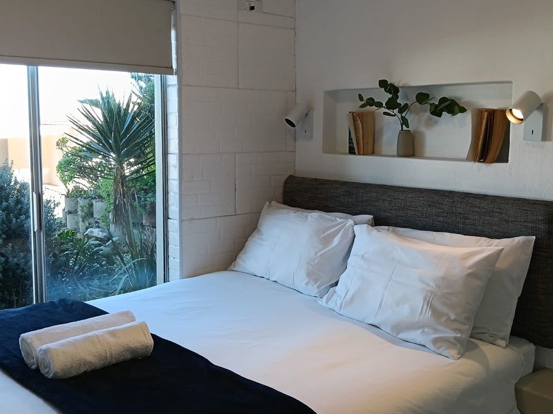 A cozy bedroom featuring a painted brick wall, a built-in recessed niche for storage, and a sliding glass door providing access to the garden.