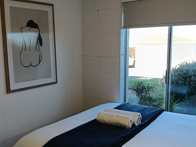 A bedroom featuring a sliding glass door with a roller blind and a painted brick wall, offering natural light and garden views.