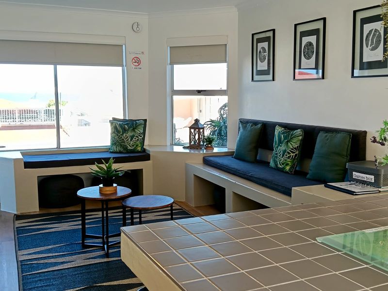 A bright living area featuring built-in bench seating, tiled counter space, and large windows with roller blinds, offering a functional and comfortable layout.