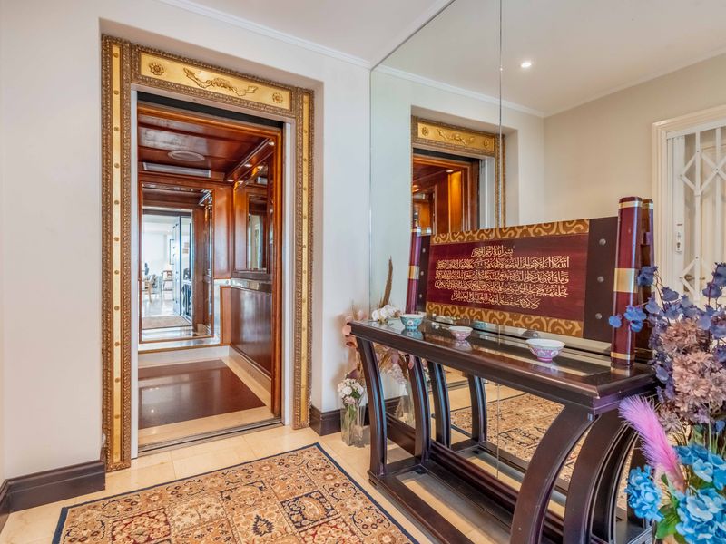 Elegant penthouse entrance featuring a private elevator with ornate gold-trimmed detailing, stone flooring, and a large wall-mounted mirror.