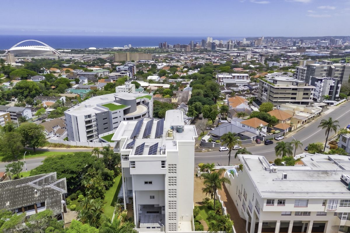 Aerial view of the penthouse building featuring rooftop solar panels, surrounding landscaped gardens, and proximity to the city skyline and coastline.