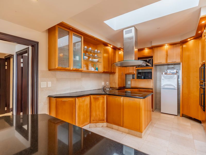 A well-appointed kitchen featuring warm wooden cabinetry, black granite countertops, integrated appliances, and a large skylight providing ample natural light.