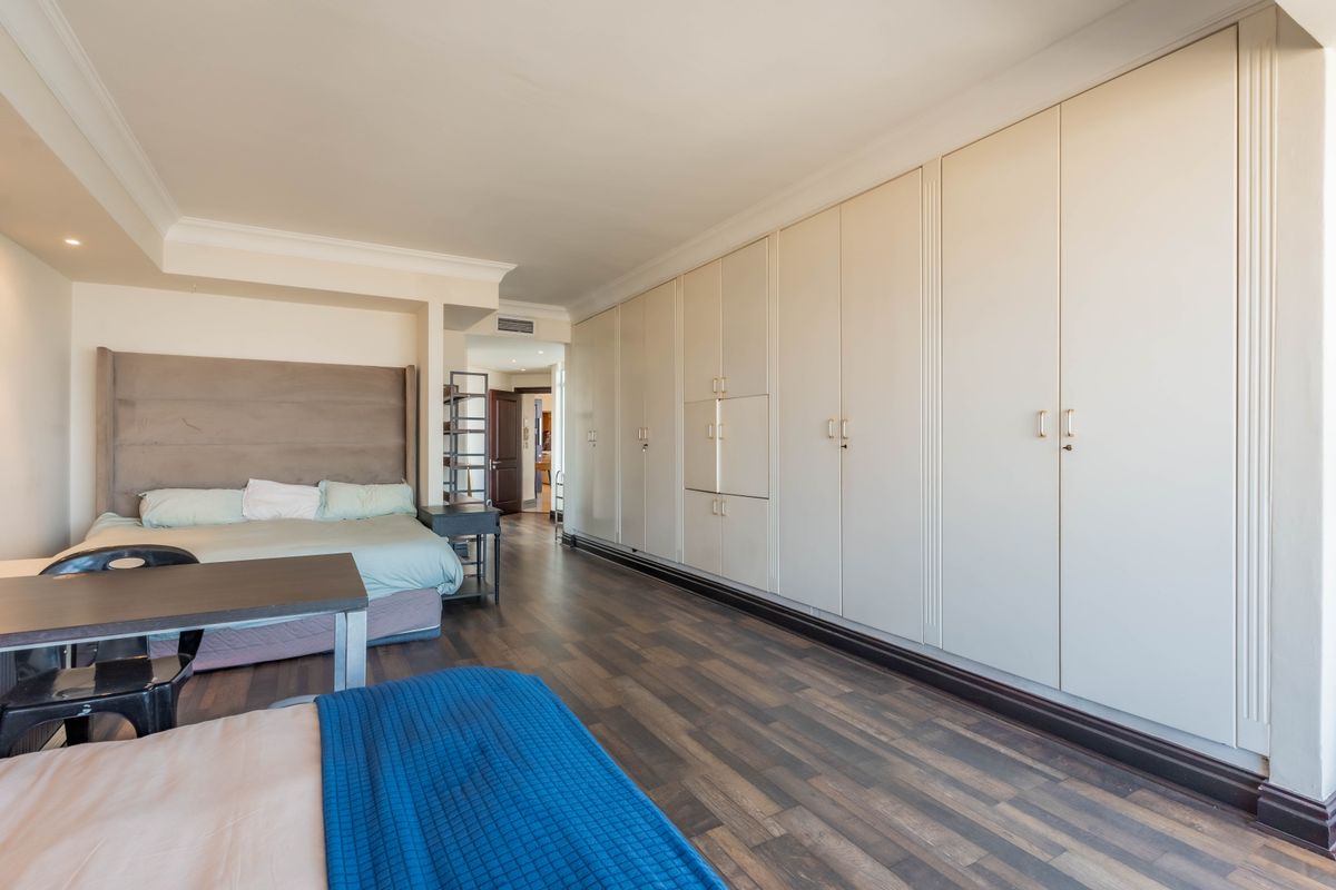 Spacious bedroom featuring extensive floor-to-ceiling built-in cupboards, dark laminate flooring, and integrated air conditioning.