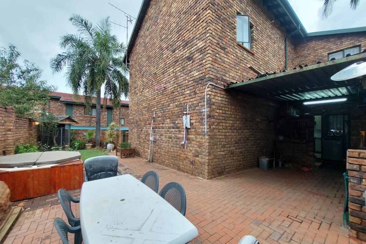 Rear exterior view of the townhouse featuring a brick facade, paved patio area, and a covered outdoor space.