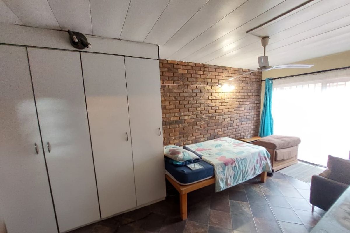 Bedroom featuring an exposed brick feature wall, built-in cupboards, tiled flooring, and a ceiling fan with access to natural light.