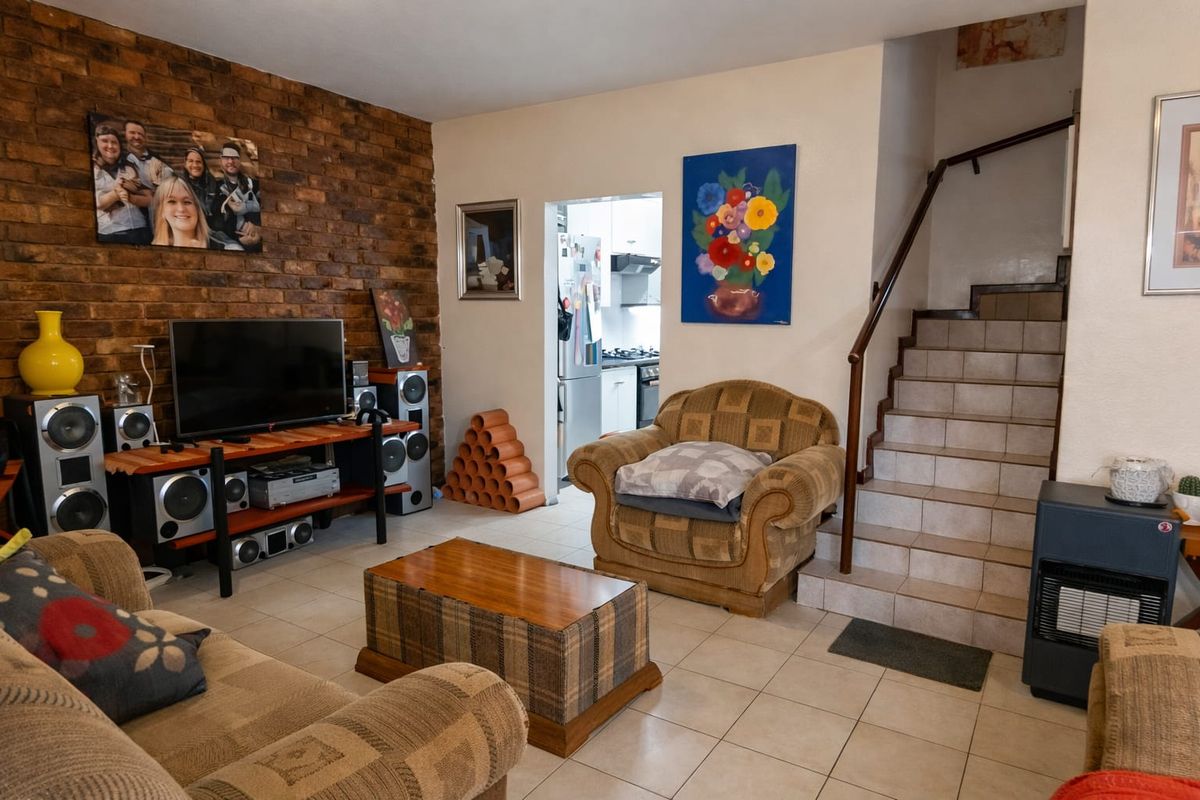 Living room featuring an exposed brick wall, tiled flooring, and a staircase leading to the upper level, with an adjacent view into the kitchen.