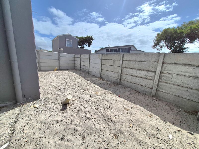 A rear outdoor area featuring a precast concrete boundary wall and unlandscaped sandy ground, offering potential for garden development.