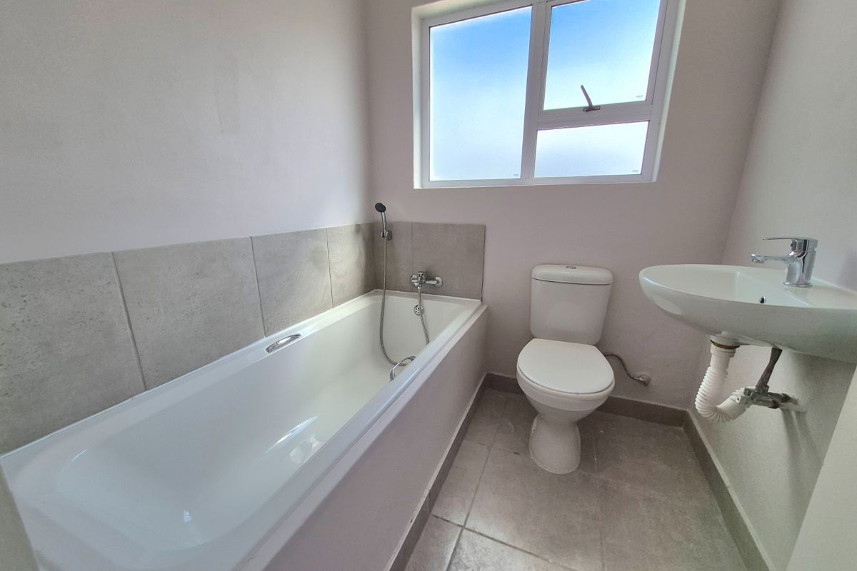 A functional bathroom featuring a bathtub, toilet, and wall-mounted basin with tiled flooring and splashbacks, offering a clean and neutral space.