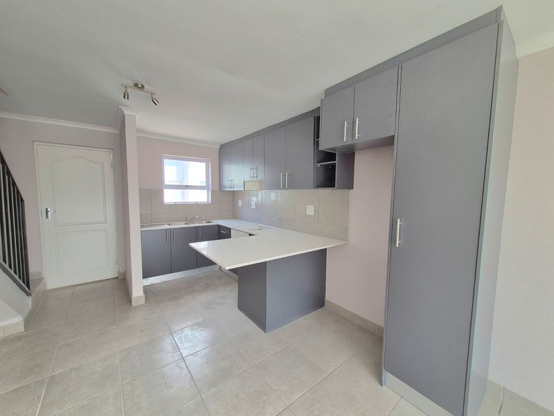 Modern kitchen featuring grey cabinetry, white stone countertops, tiled backsplash, and a breakfast bar, presented in a clean, empty space.