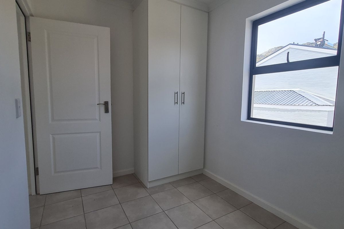 A clean, empty bedroom featuring neutral tiled flooring, a built-in wardrobe, and a window with natural light.