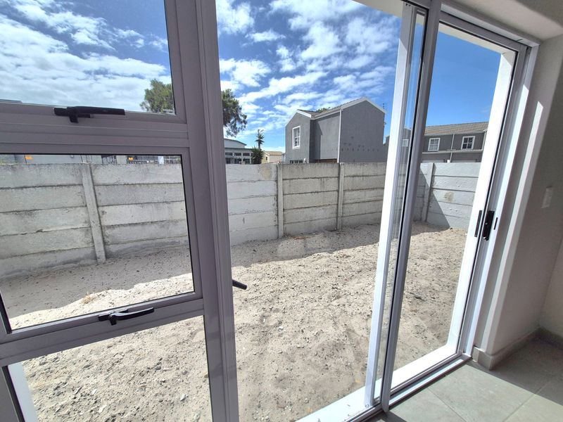 View from the interior through sliding glass doors looking out onto an unlandscaped rear courtyard with a precast concrete boundary wall.