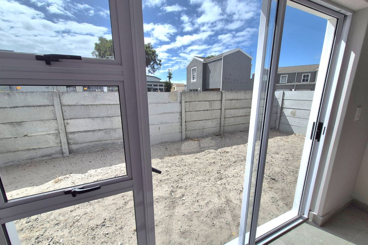 View from the interior through sliding glass doors looking out onto an unlandscaped rear courtyard with a precast concrete boundary wall.