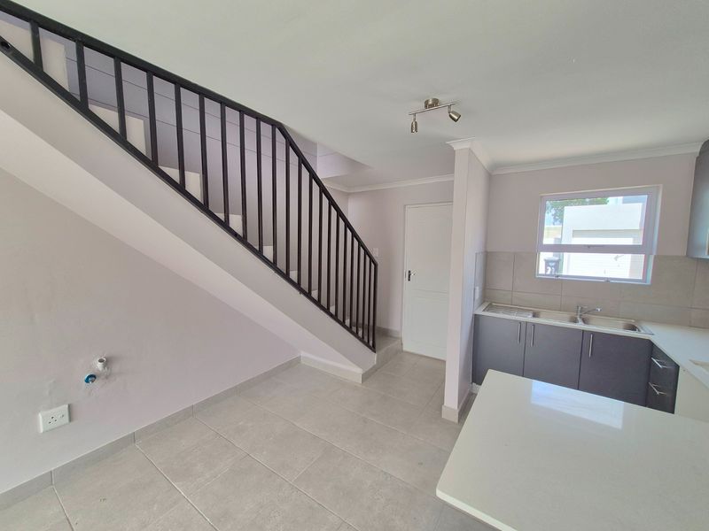 Open plan kitchen area featuring modern cabinetry, tiled flooring, and a staircase with a metal balustrade leading to the upper level.