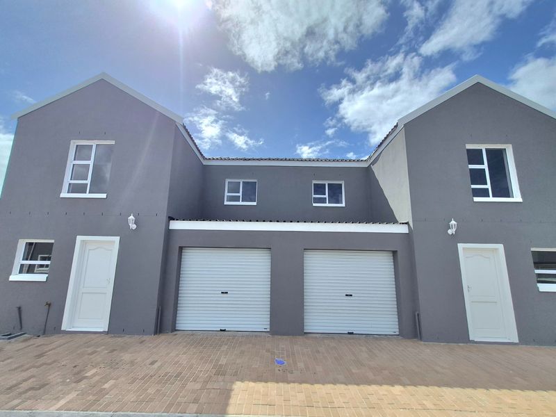 Front elevation of a modern townhouse featuring a double garage with roller shutter doors and a paved driveway.