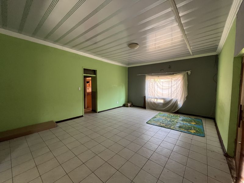An empty living room featuring tiled flooring and a panelled ceiling, offering a blank canvas for renovation and interior design updates.