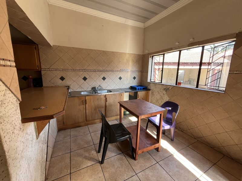 A dated kitchen featuring wooden cabinetry, tiled splashbacks, and tiled flooring, requiring cosmetic updates to modernize the space.