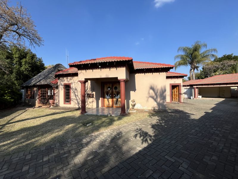 Front elevation of a house featuring a tiled roof, thatched section, paved driveway, and a covered entrance porch with decorative columns.