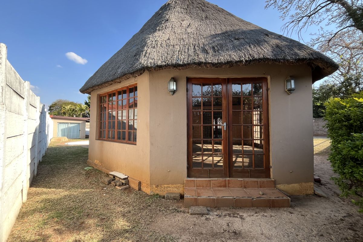 A detached garden structure featuring a traditional thatch roof, timber-framed french doors, and windows, set within a private backyard area.