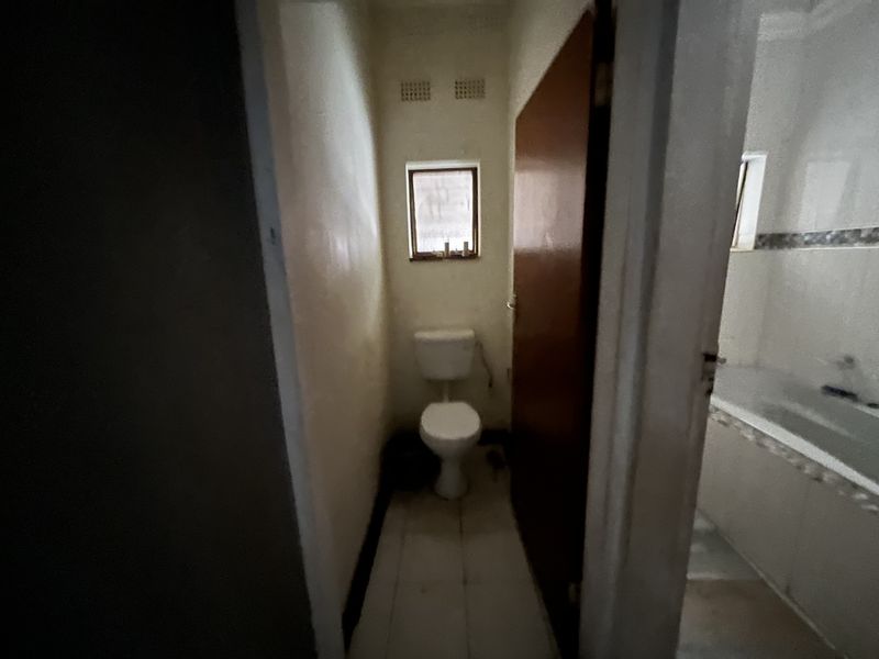 A small, dated bathroom featuring a separate toilet area and a bathtub, requiring modernization and improved lighting.